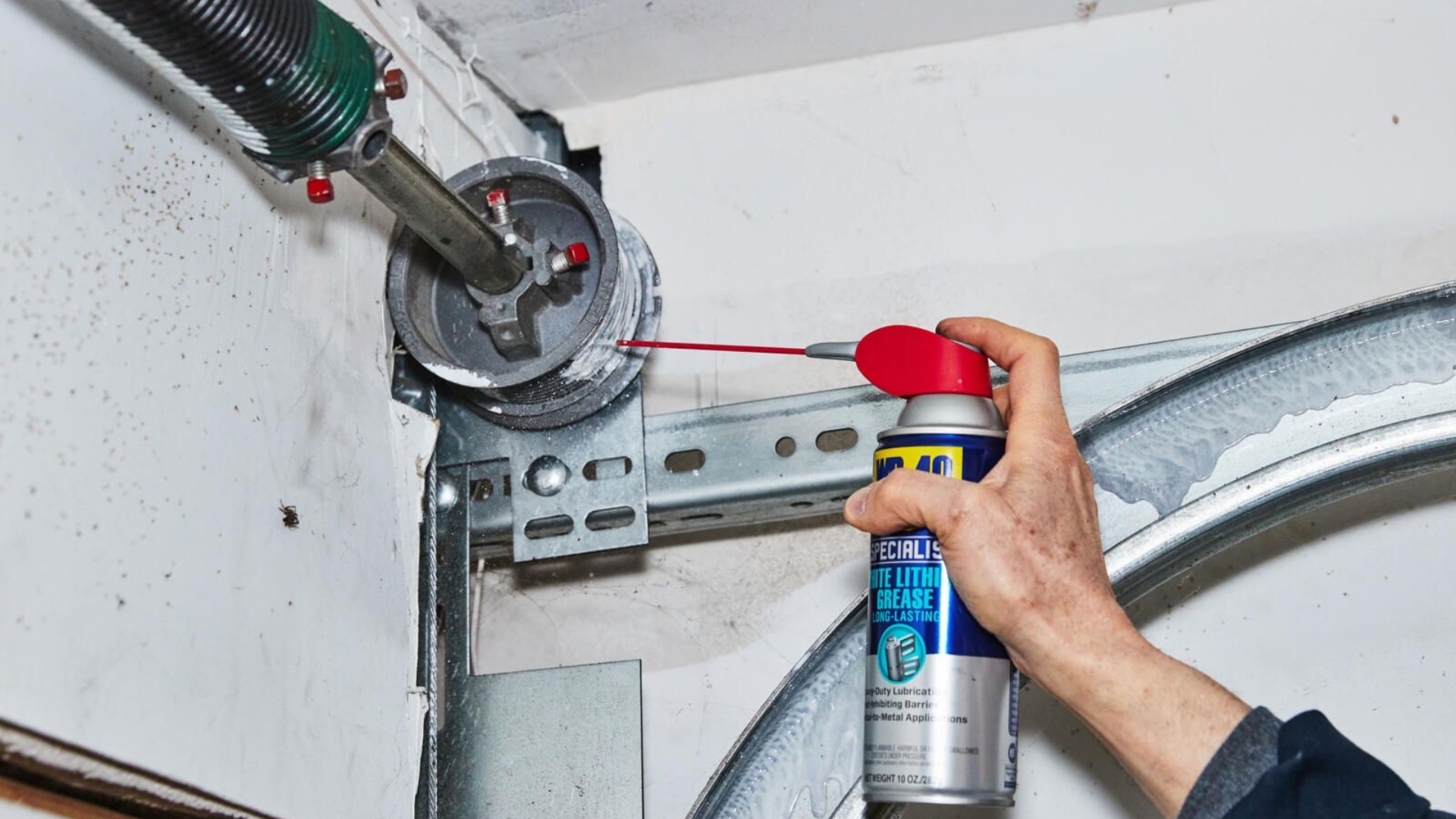 A user applying garage door lubricant on cable drum