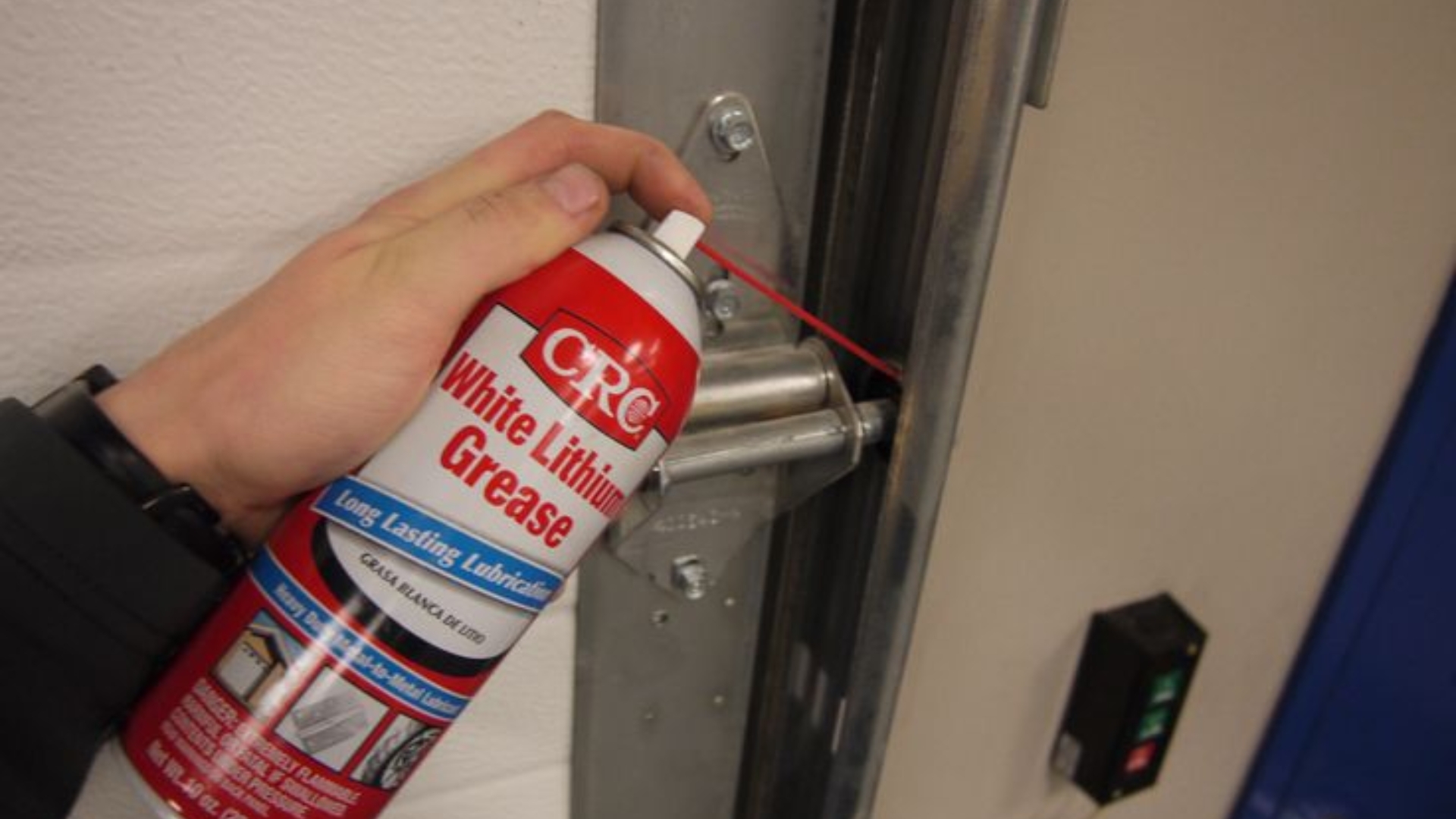 A user applying garage door lubricant on the rollers