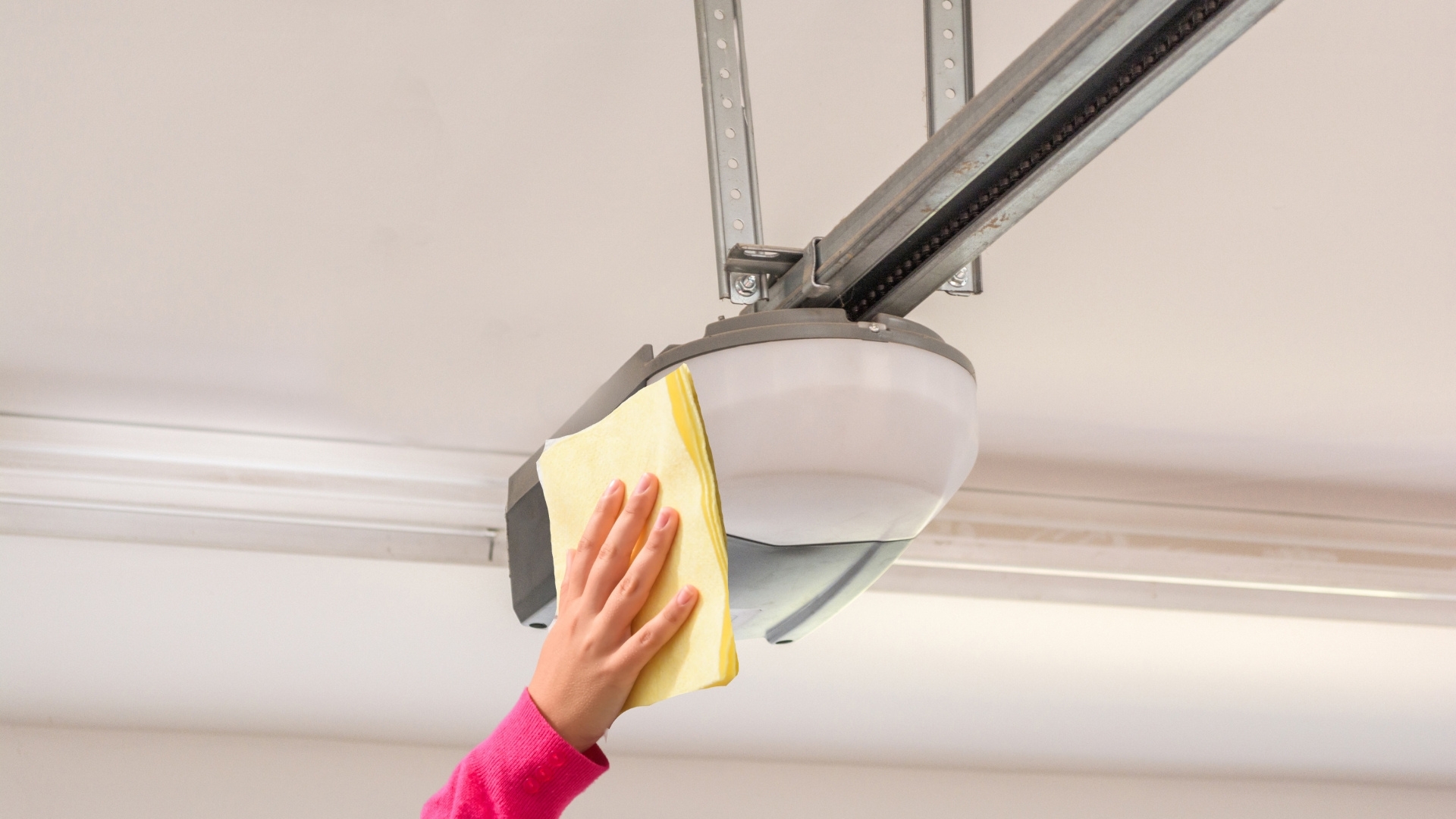 A user wiping the case of an opener during garage door opener maintenance