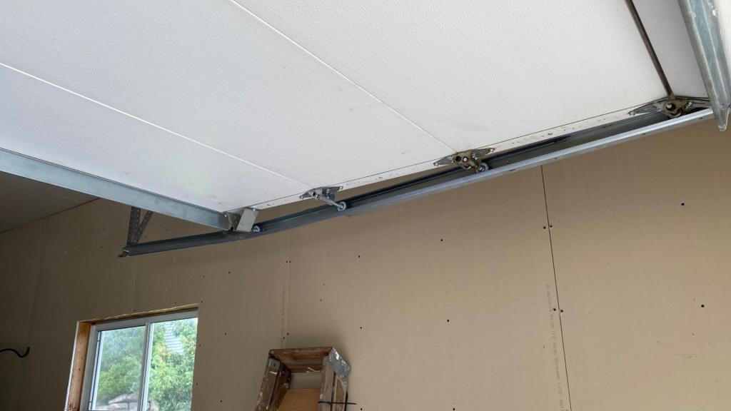 Close-up view of a garage door with a torsion spring installed above it, showing the spring mechanism and mounting brackets