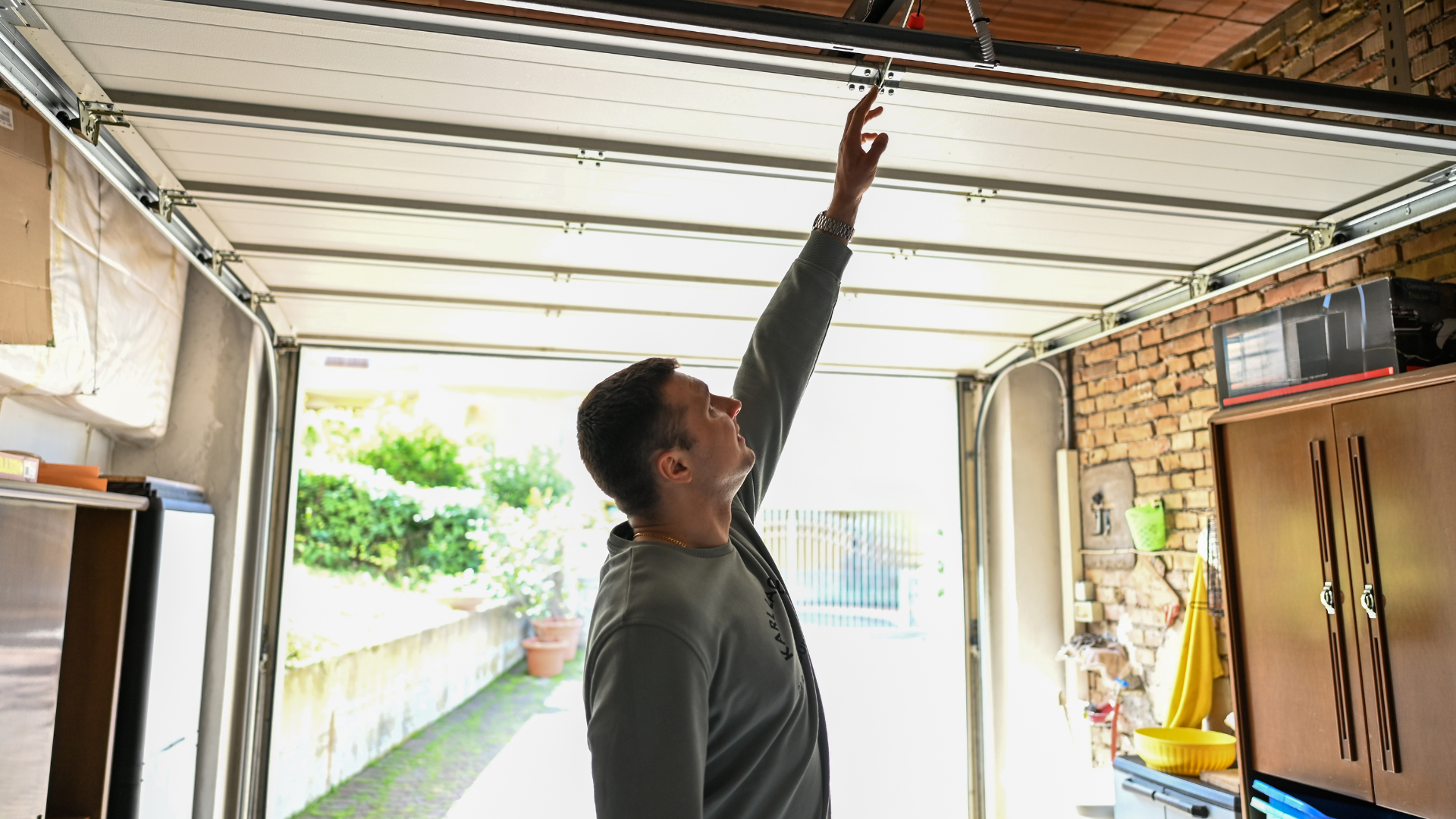 Man performing garage door maintenance in a Valley Village garage, inspecting and adjusting the overhead springs and tracks to ensure smooth, safe, and reliable door operation.