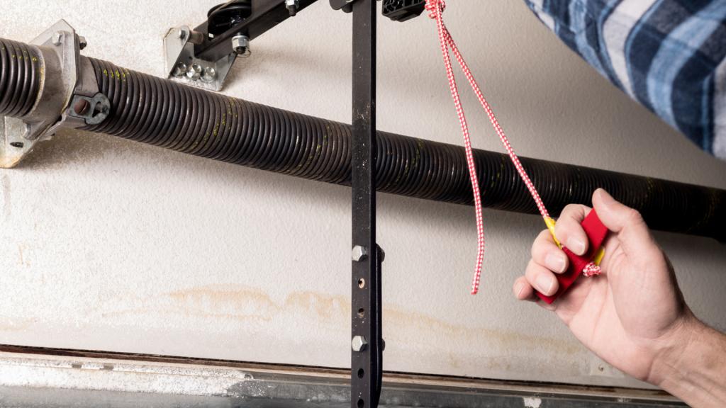 Person pulling the garage door emergency release handle beside the torsion spring system